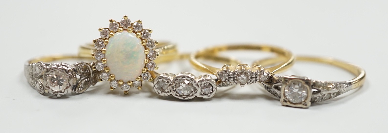 Four assorted 18ct and gem set dress rings, including white opal and diamond and two three stone diamond and one yellow metal and single stone diamond set ring, gross weight 14.3 grams.
